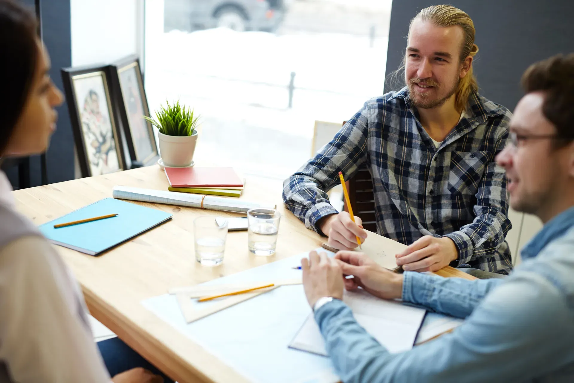 Drie mensen overleggen geconcentreerd aan een tafel met notitieboeken